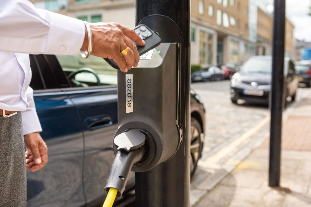 Person plugging an electric vehicle into a charging station on a city street.