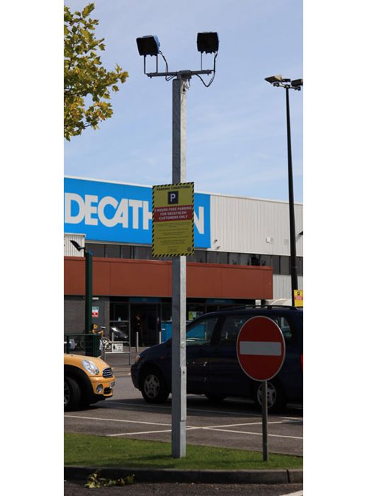 Galvanised steel CCTV column with dual camera mounts and parking sign in retail car park, suitable for 3m–12m installations.