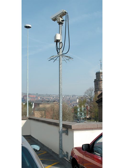Wall-mounted CCTV camera pole with anti-climb guard, installed in a car park for urban surveillance and security monitoring.